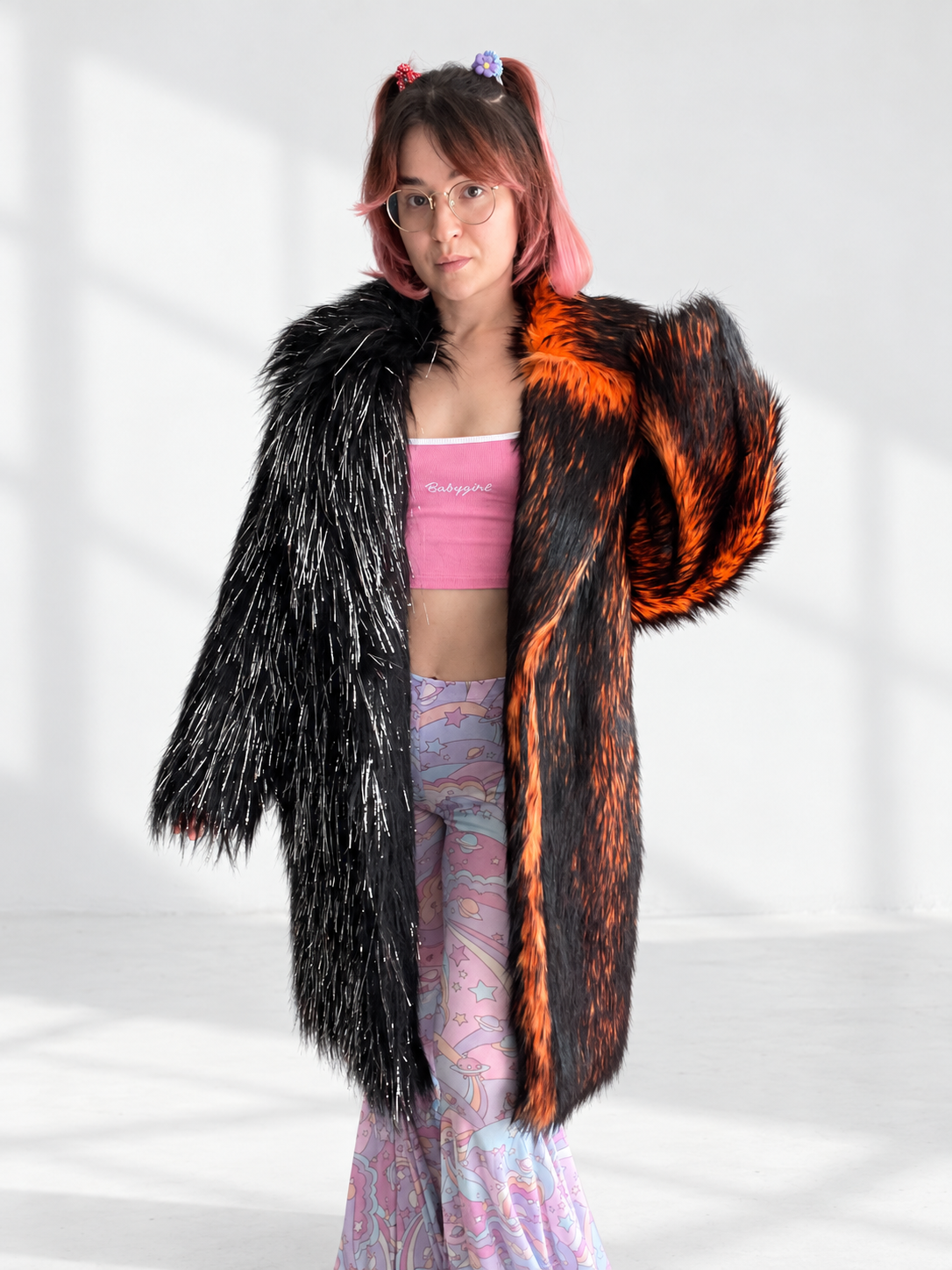 A model posing in a long, oversized faux fur coat with contrasting black shiny tinsel fur and fiery orange-and-black shag fur, featuring wide sleeves and an open front.