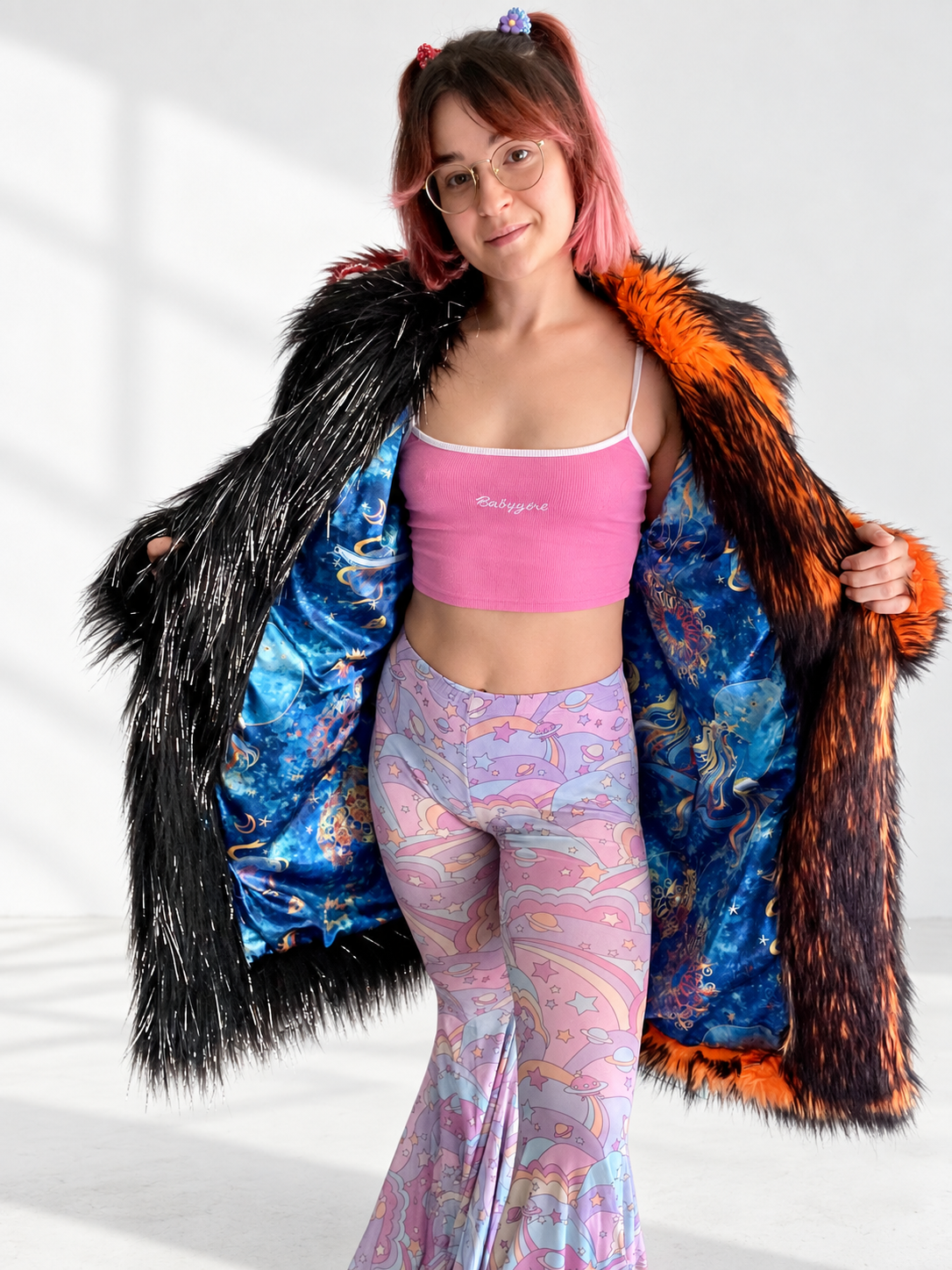 A model holding open an oversized black and fiery orange faux fur coat to reveal its vibrant blue celestial satin lining with sun, moon, and star patterns.